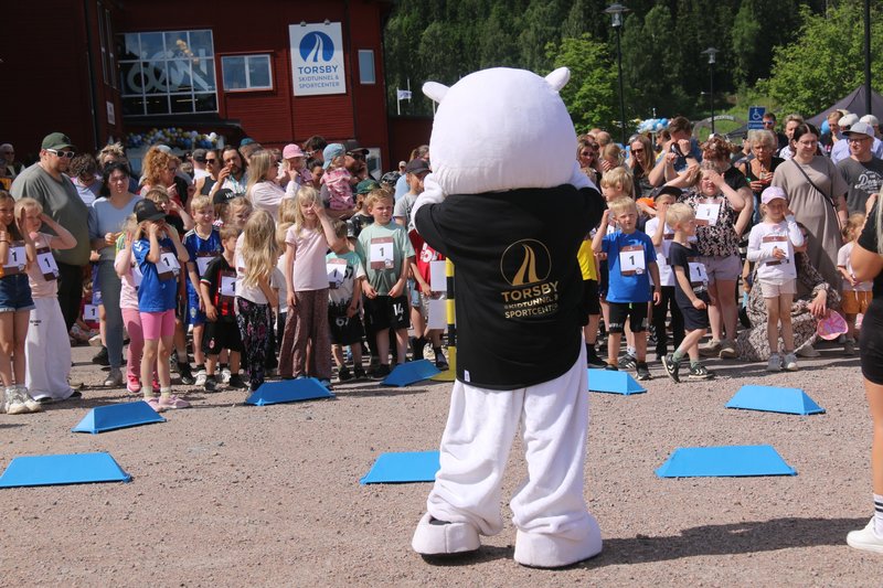 En lurvig björn (en maskot) och många barn som värmer upp inför ett lopp