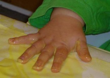 En barnhand som är full med målarfärg på papper